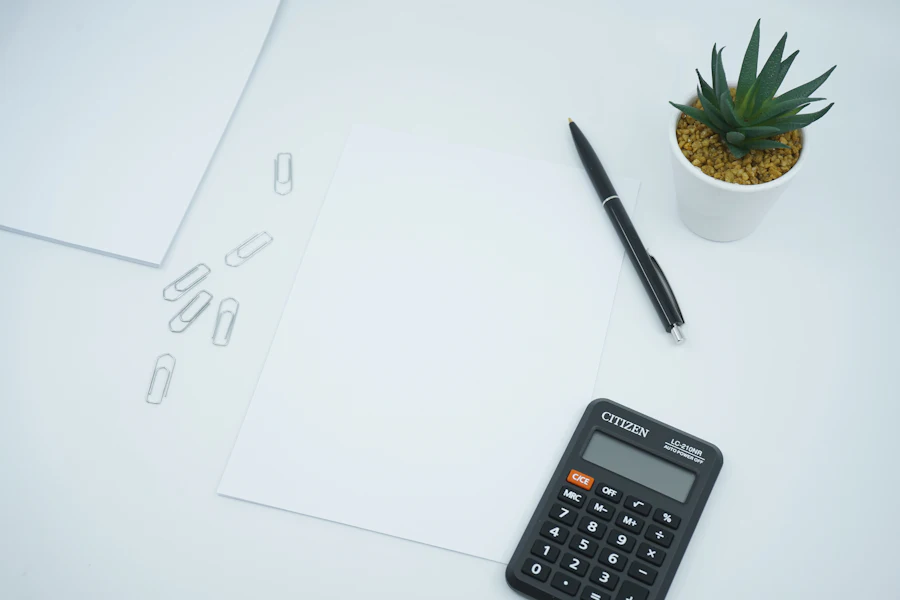 Calculator, pen, paper clips and a small plant on a white desk