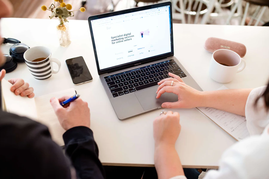 Hands at a shared desk with a laptop, coffee cups and notes