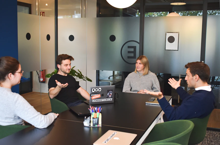 Four colleagues talking around a table in a glass-walled meeting room