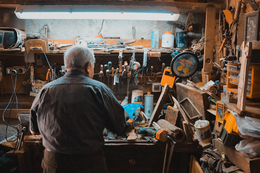 Man at a workbench in a crowded machine workshop, seen from behind